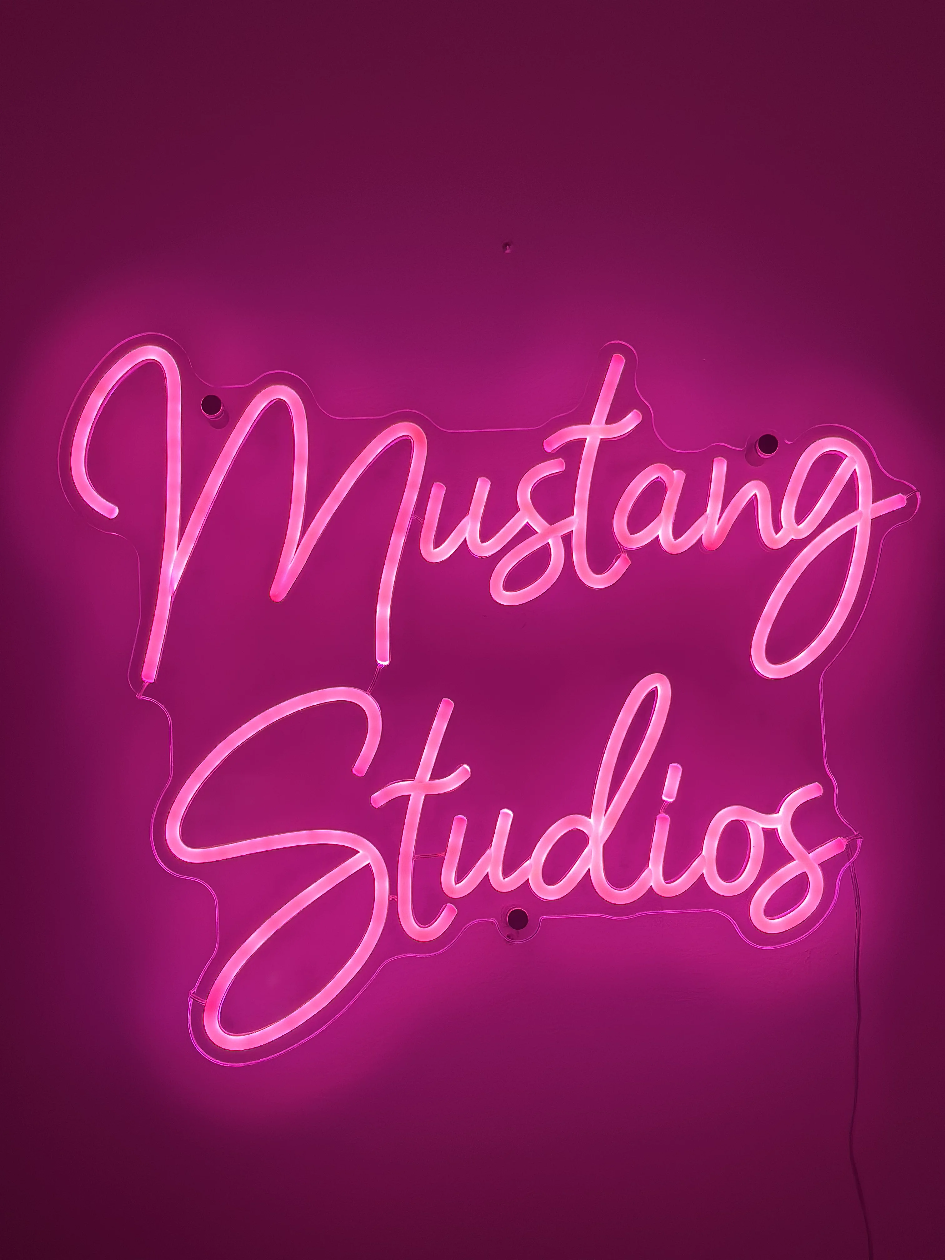 Pink neon 'Mustang Studios' sign glowing on a deep magenta wall